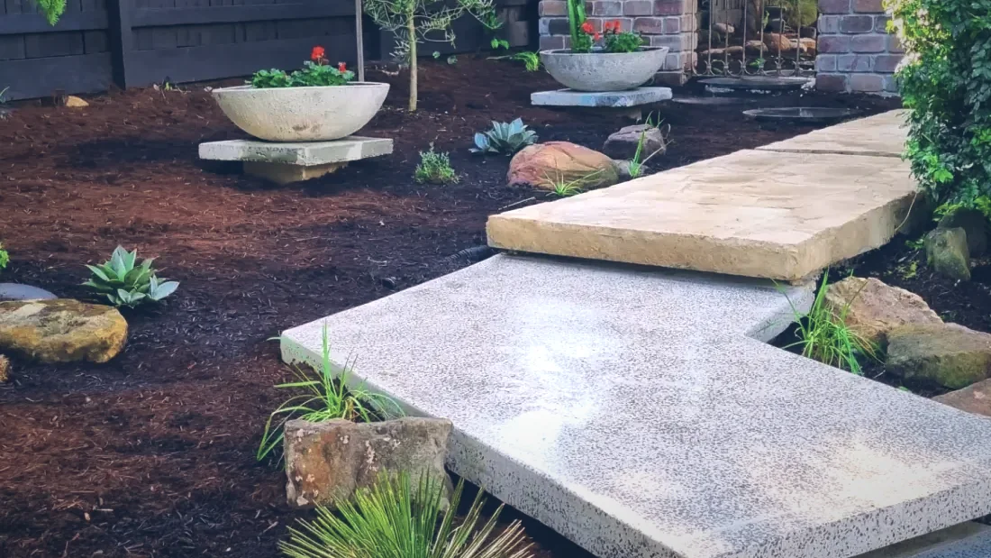 Thick sandstone slab stepping stones set into black mulch between cast feature bowls and brick pillars