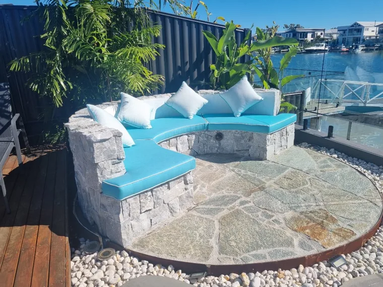 A crazy paved seating circle with a curved stone bench and blue cushions, set above a canal