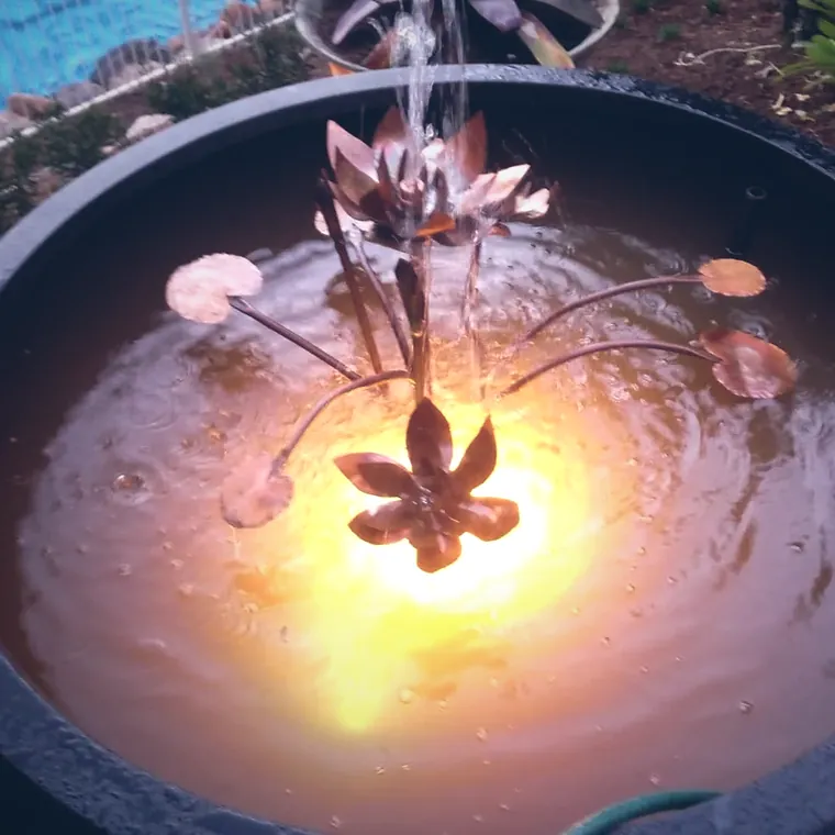 Copper water bowl with a lit sculptural fountain spilling at night