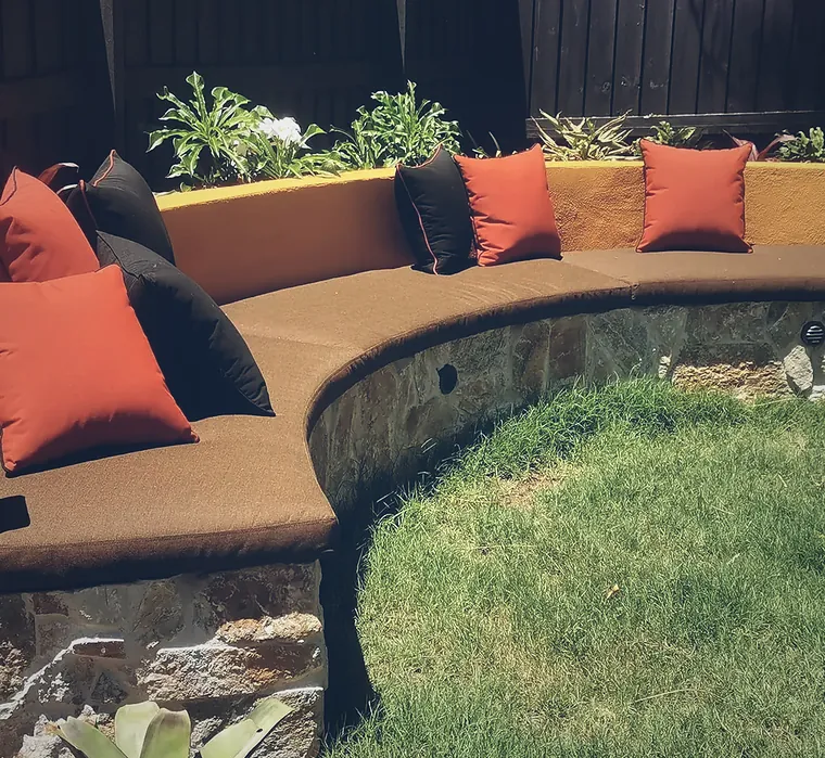 Curved sandstone bench seat with cushions wrapping a circle of lawn
