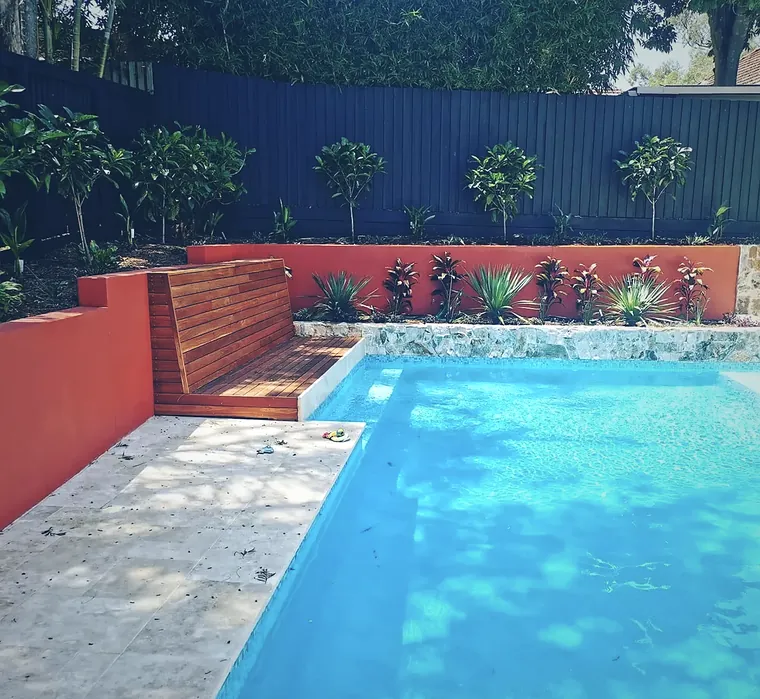 Pool edged with orange rendered walls, stone and a timber bench