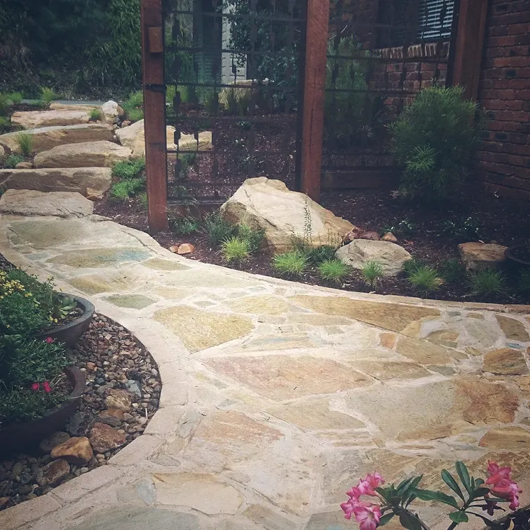Curving sandstone crazy paving path edged with boulders and garden beds