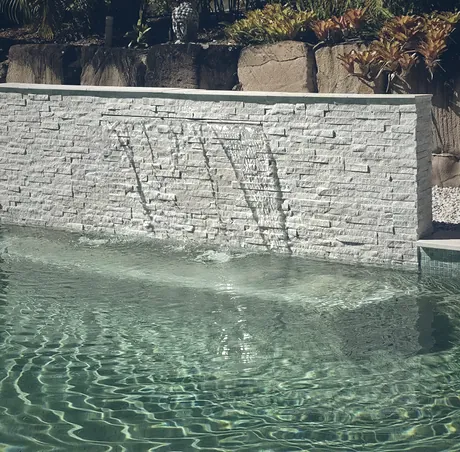 Stacked stone water wall spilling through three spouts into a pool