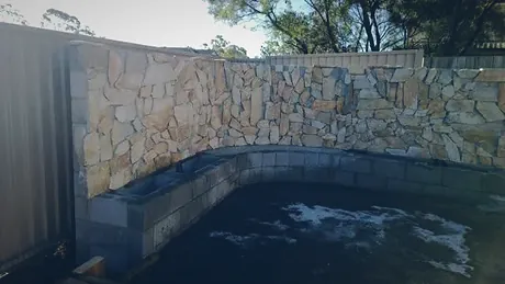 Curved natural stone wall retaining a dark garden pond