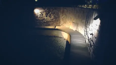 Warm uplighting on a natural stone wall beside a curving pale path at night