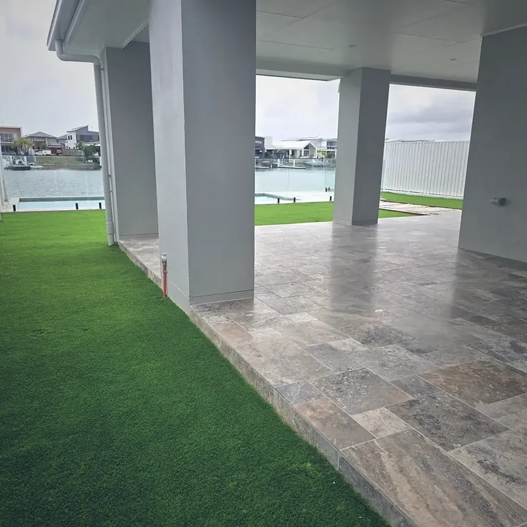 New lawn running up to a travertine terrace under a house