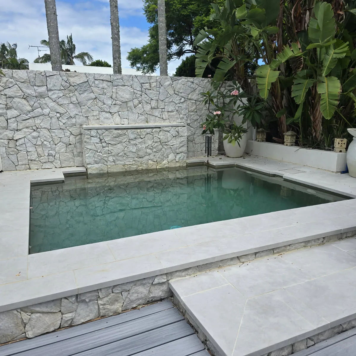 Square plunge pool edged in limestone coping with a stacked stone feature wall, water blade and frangipani