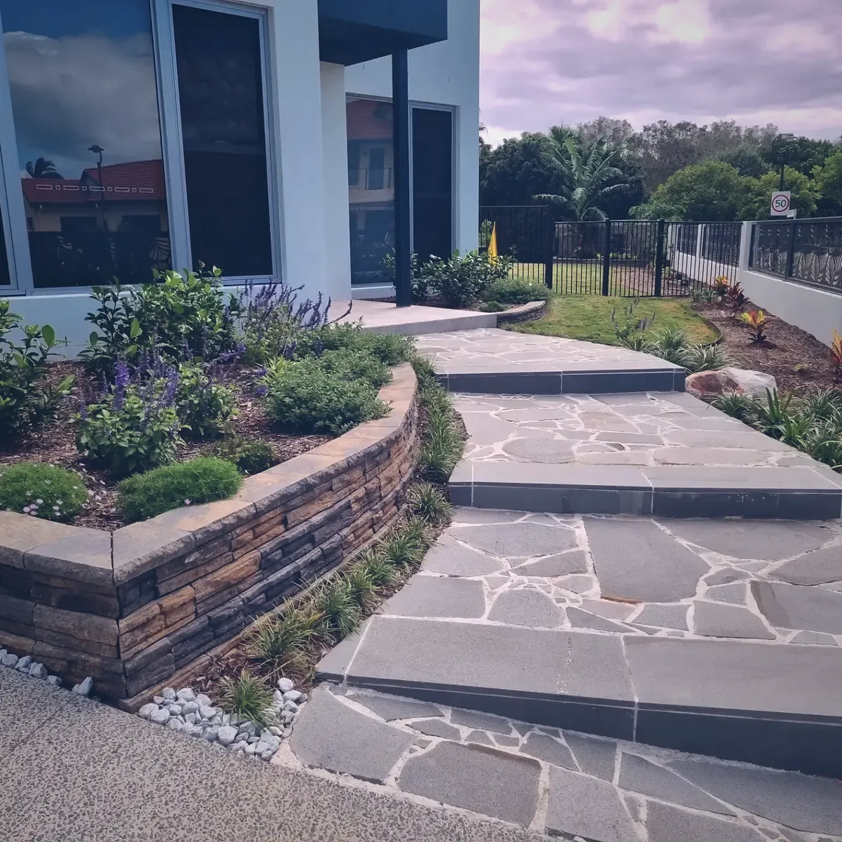 Sandstone crazy paving path beside a stacked stone retaining wall and lavender planting