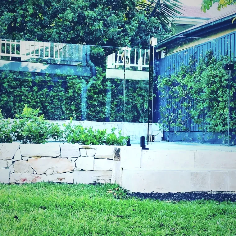 Two levels of stacked sandstone garden wall with clipped hedging behind
