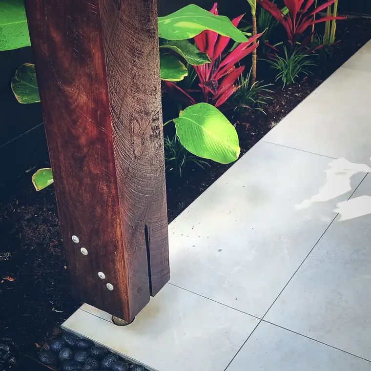 Weathered Corten steel blade standing beside a concrete path and tropical planting