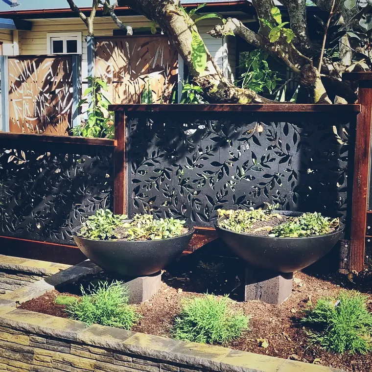 Three planted charcoal bowls in front of Corten framed laser-cut screens