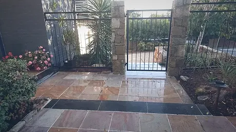 A crazy paved entry courtyard leading up to a stone pillar and steel gate